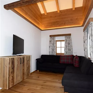 Ein gemütlicher Wohnraum mit einem schwarzen Sofa und einem Holztisch. Die Holzdecke sorgt für eine warme Atmosphäre.