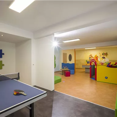 A playroom with a ping pong table and colorful walls. In the background, there is a play area for children with various toys.