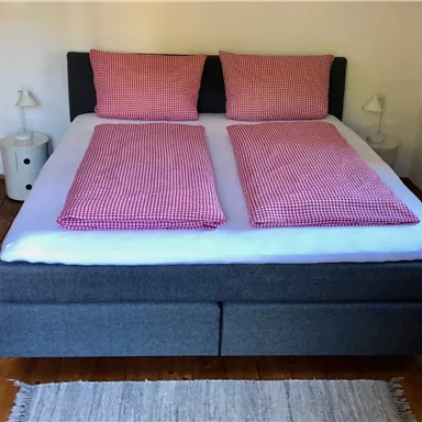 Ein gemütliches Schlafzimmer mit einem großen Doppelbett und karierter Bettwäsche. Neben dem Bett stehen zwei Nachttische mit Lampen.