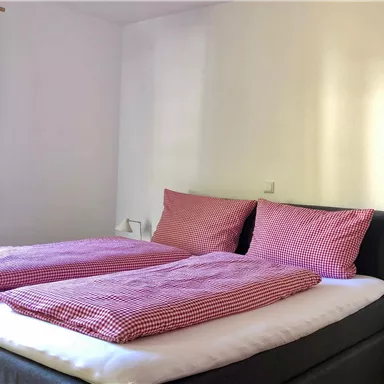 Ein gemütliches Schlafzimmer mit einem Doppelbett und karierten Bettdecken. Die grünen Vorhänge sorgen für eine einladende Atmosphäre.