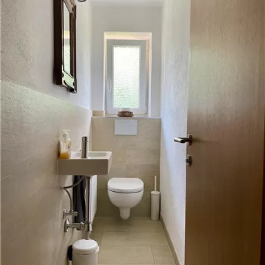 Ein modernes Badezimmer mit einem kleinen Fenster und einer hellen, freundlichen Atmosphäre. Es enthält ein Waschbecken, eine Toilette und dekorative Elemente.