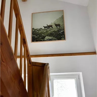 Ein Treppenhaus mit Holzhandlauf und einer Fensterbank. An der Wand hängt ein Gemälde von Rehen in einer Landschaft.