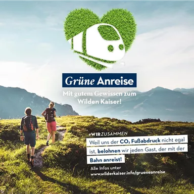 Two hikers explore a mountain landscape with green meadows and high mountains in the background. The graphic promotes eco-friendly travel by train to the Wilder Kaiser.