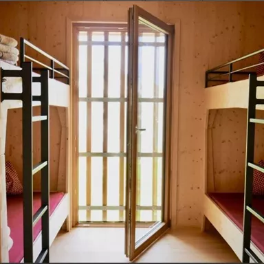 A cozy sleeping area with two bunk beds and bright wooden walls. The open door offers a view of the outside world.