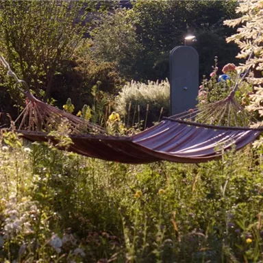 A hammock swings gently between trees in a blooming garden. Surrounded by lush greenery and colorful flowers, the place offers a tranquil atmosphere.
