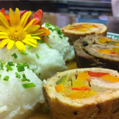 Ein köstliches Gericht mit gefülltem Fleisch und buntem Gemüse. Dazu serviert sind beiger Reis und ein Essensblumen-Dekor.