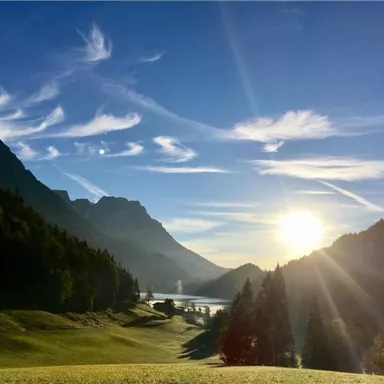 Eine malerische Landschaft mit Bergen und einem klaren Himmel. Die Sonne scheint über die sanften Hügel und einen See.