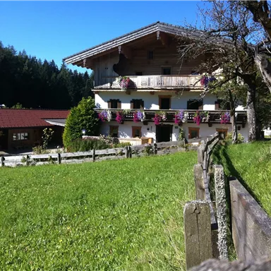 Ein malerisches Landhaus mit Blumenkästen und einem großen Garten. Die Umgebung ist grün und von Bäumen umgeben.