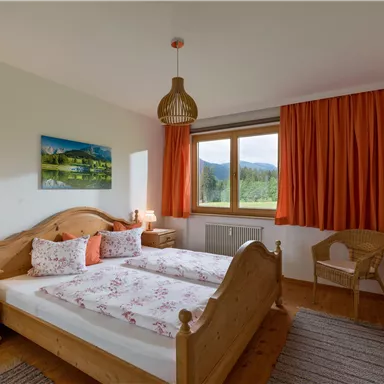 Ein gemütliches Schlafzimmer mit zwei Betten und einem Holzrahmen. Große Fenster lassen viel natürliches Licht herein und bieten einen Blick auf die Landschaft.