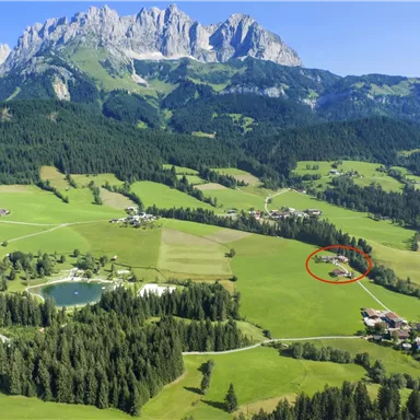 Eine wunderschöne Landschaft mit Bergen, Wäldern und grünen Wiesen. Im Vordergrund sind ein Teich und ein kleiner Ort zu sehen.