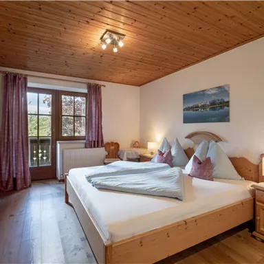 A cozy bedroom with wood paneling and a large window. There is a double bed with comfortable pillows and pleasant lighting.