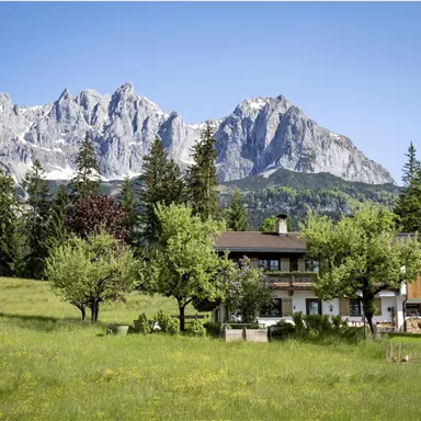 A picturesque landscape with green meadows and a charming accommodation. Majestic mountains rise in the background.