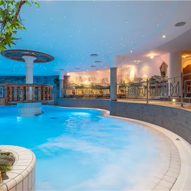 An elegant indoor pool with gentle curves and a beautiful plant arrangement. The atmosphere is enhanced by the shimmering lights on the ceiling.