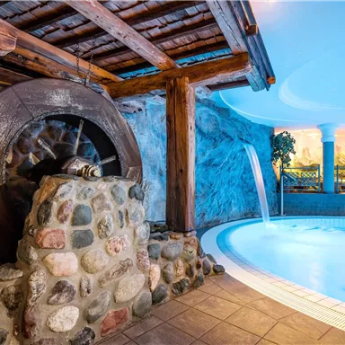 A relaxing indoor pool with natural stone and rustic wooden elements. The water flows gently into the pool landscape.