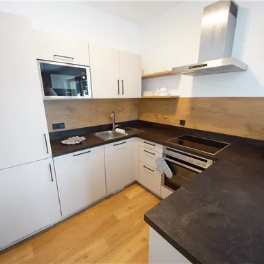 Eine moderne Küche mit hellen Schränken und einem dunklen Arbeitsbereich. Die Ausstattung umfasst einen Herd, eine Spüle und einen Wasserkocher.