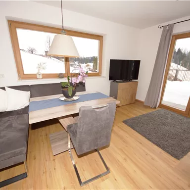 Ein gemütlicher Wohnbereich mit modernen Möbeln und einem großen Fenster. Der Raum ist hell und freundlich, ideal für Entspannung.