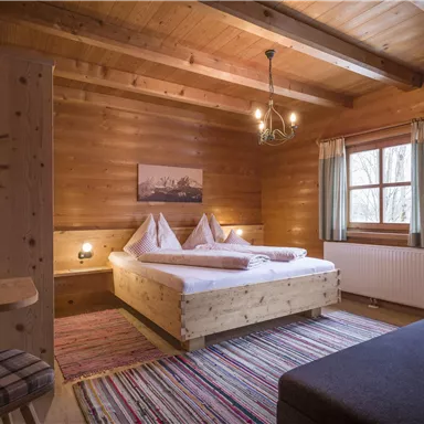 Ein gemütliches Schlafzimmer aus Holz mit einem großen Bett und zwei Kissen. Die Wände sind aus Holz und es gibt ein Fenster mit Vorhängen.