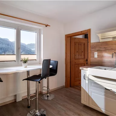 A modern kitchen with a white sink and stylish bar stools. Large windows provide a view of the mountains in the background.