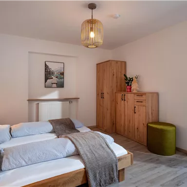 A cozy bedroom with a wooden bed and a modern lamp. The room is bright and minimally furnished, with a large window front and a beautiful view outside.