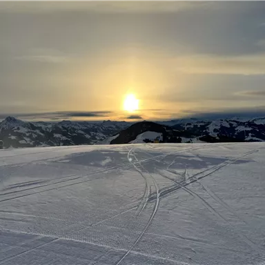 Ein wunderschöner Sonnenuntergang über verschneiten Bergen. Der Himmel ist bewölkt und friedlich.