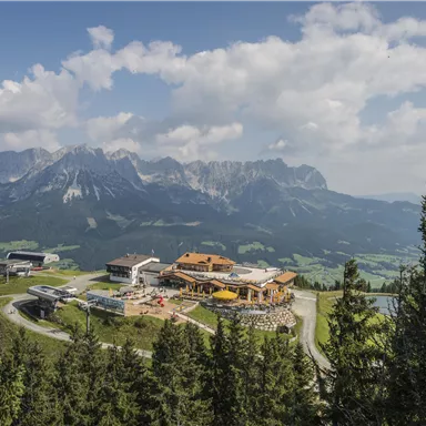Eine malerische Berglandschaft mit einem Restaurant auf einem Höhenzug. Im Hintergrund sind majestätische Berge und ein blauer Himmel zu sehen.