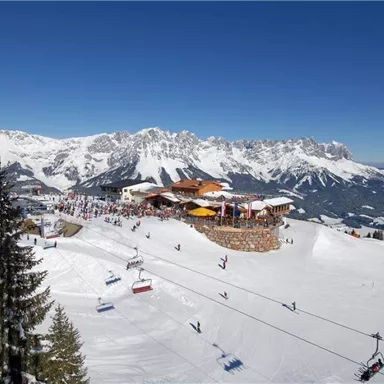 An impressive mountain landscape with snow-covered slopes and a cozy restaurant. Skiers enjoy the sun and the clear view.