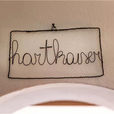 Eine Drahtschrift mit dem Wort "Harthauser" hängt an der Wand. Der Hintergrund ist schlicht und hell.