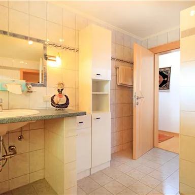 A bright bathroom with tiled walls and a large mirror. There is a shower and modern furniture that offers space.