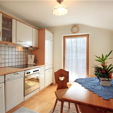A modern kitchen with bright cabinets and a dining table. On the table is a plant and there is a large window that lets in plenty of light.