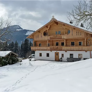 Ein gemütliches Holzhaus im Schnee mit einer malerischen Berglandschaft im Hintergrund. Die Umgebung ist ruhig und winterlich, mit schneebedeckten Bäumen.