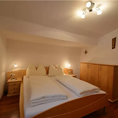 A cozy bedroom with a double bed and wooden wardrobes. The walls are in light colors, and the light is warm and inviting.
