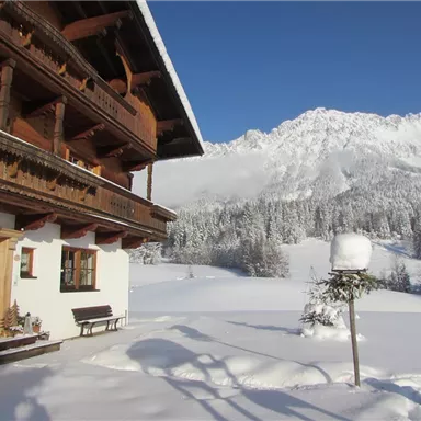 A cozy chalet in winter, surrounded by a lot of snow. Majestic mountains rise in the background under a clear sky.