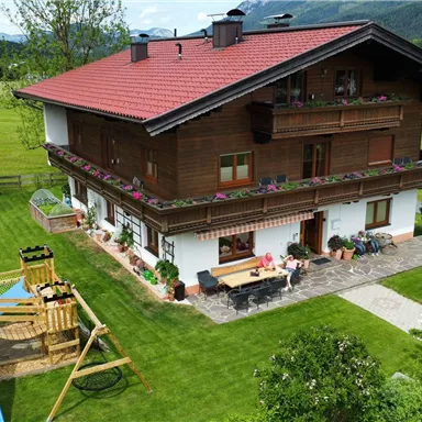 Ein schönes, traditionelles Haus mit einem roten Dach und Balkon. Der Garten ist grün und einladend, mit Spielmöglichkeiten und einem kleinen Pool.