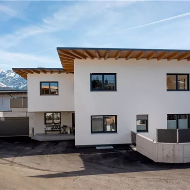 A modern building with a white facade and wood details. Snow-covered mountains are visible in the background.