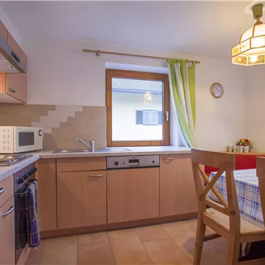 A cozy kitchen with wooden cabinets and modern appliances. A dining table with chairs is next to a window with a view outside.