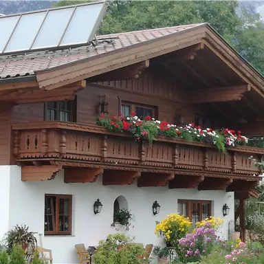 Ein traditionelles Holzhaus mit einem Blumengarten und einem Balkon. Auf dem Dach sind Solarpanels installiert.