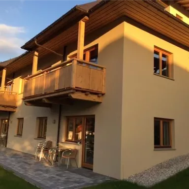 Ein modernes Haus mit Holzbalcon und großen Fenstern. Der Außenbereich ist mit Rasen und Steinen gestaltet.