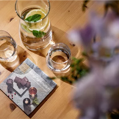 A table with a jug of water, two glasses, and a menu card. Flowers can be seen in the background.