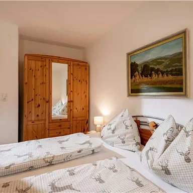 A cozy bedroom with two single beds and rustic wooden furnishings. A large wardrobe and a picture on the wall complete the pleasant atmosphere.