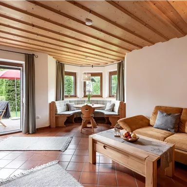 Cozy living room with wooden beam ceiling and a large window. There is a comfortable sofa and a dining table with benches.
