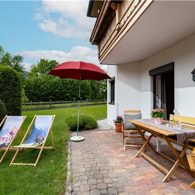 A cozy outdoor area with two loungers and a sun umbrella. The table is set for a relaxing meal outside.