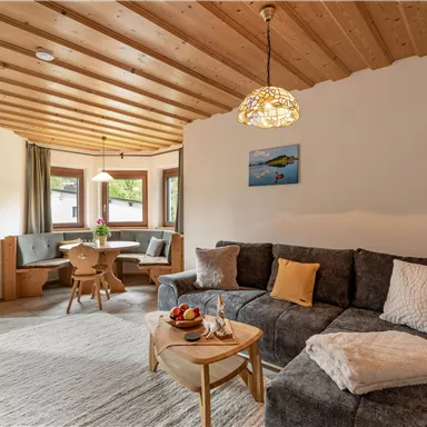 A cozy living room with a modern sofa and a wooden table. Large windows provide plenty of daylight and an inviting atmosphere.