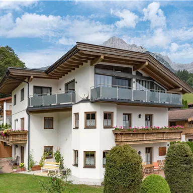A modern house in a rural setting, surrounded by trees and mountains. The sky is slightly cloudy, creating a calm atmosphere.