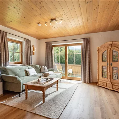 A cozy living room with a wood stove, a sofa landscape, and a large window. Bright wooden details and a rug create an inviting atmosphere.