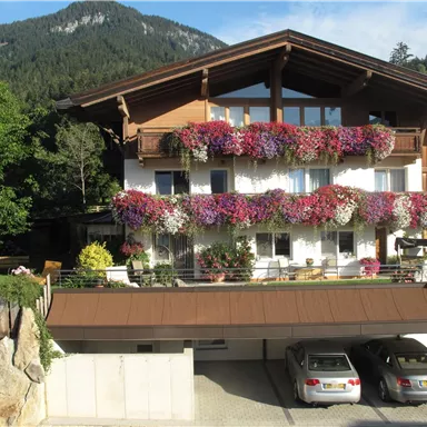 A picturesque house with flower boxes and a beautiful balcony view. In the foreground, two cars can be seen in front of a garage, and in the background, mountains stretch out.