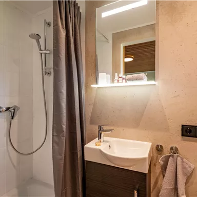 Ein modernes Badezimmer mit einer Duschnische und einem Waschbecken. Die Wände sind hell und schlicht gestaltet.