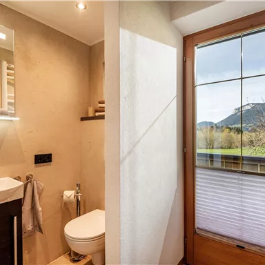 Ein modernes Badezimmer mit hellen Wänden und elegantem Waschbecken. Durch das Fenster ist eine schöne Berglandschaft zu sehen.