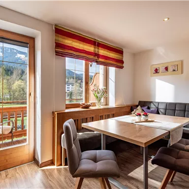 Ein gemütlicher Esstisch in einem hellen Raum mit Blick auf die Berge. Große Fenster lassen viel Licht herein und zeigen einen Balkon im Freien.