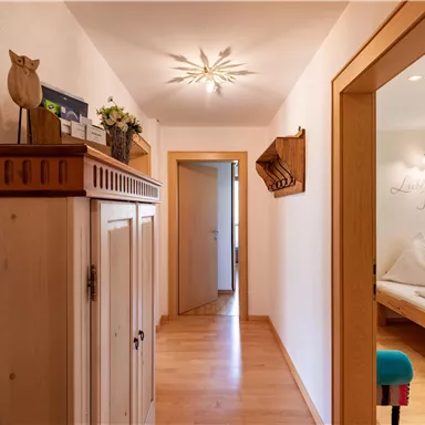 Ein heller Flur mit Holzfußboden und einem gemütlichen Schrank. Im Hintergrund sieht man ein Zimmer mit Schlafplätzen und warmem Licht.