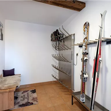 Ein Skiraum mit Skiern an einer Wandhalterung und Platz für Schuhe. An der Wand befindet sich eine Sitzgelegenheit und Holzverkleidung.